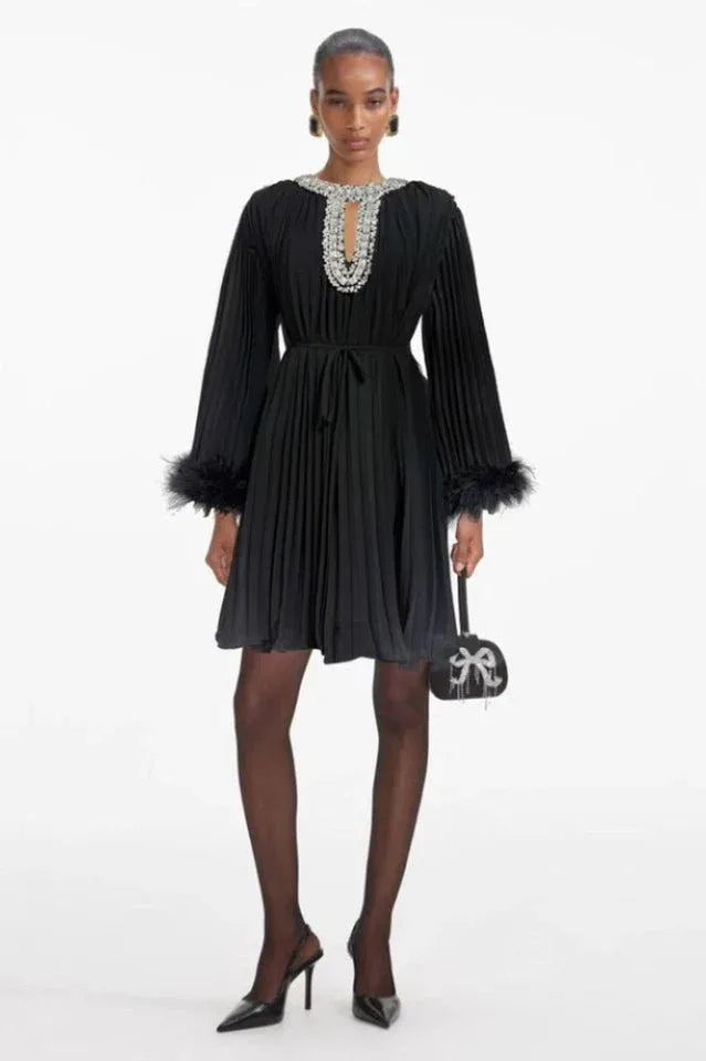woman wearing a black pleated mini dress with feather cuffs and an embellished neckline