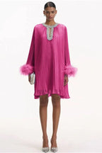 woman wearing a hot pink pleated mini dress with feather cuffs and an embellished neckline