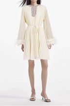 woman wearing a cream pleated mini dress with feather cuffs and an embellished neckline