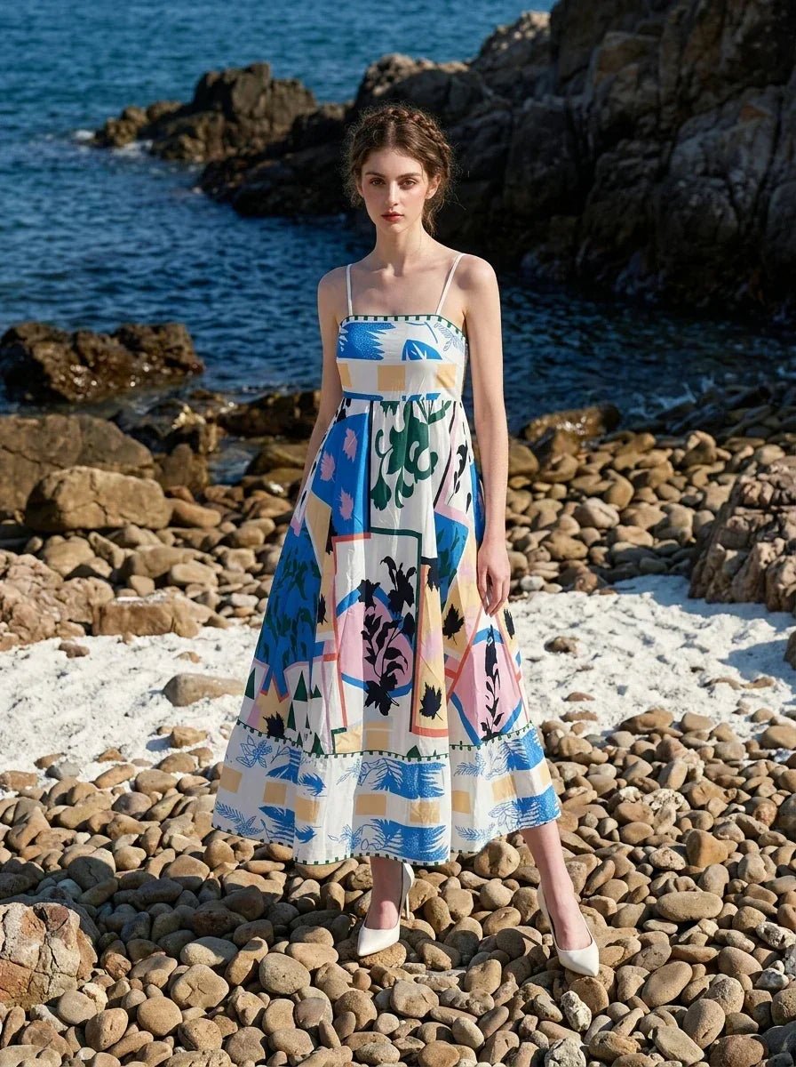 Woman wearing a midi dress with an abstract geometric print standing on a rocky beach with the ocean in the background.