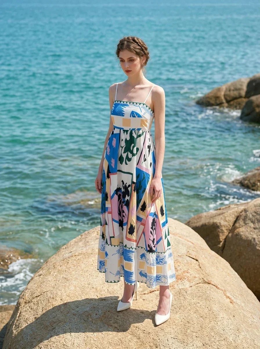 Woman wearing a midi dress with an abstract geometric print standing on a large rock with the ocean in the background.