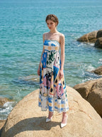 Woman wearing a midi dress with an abstract geometric print standing on a large rock with the ocean in the background.