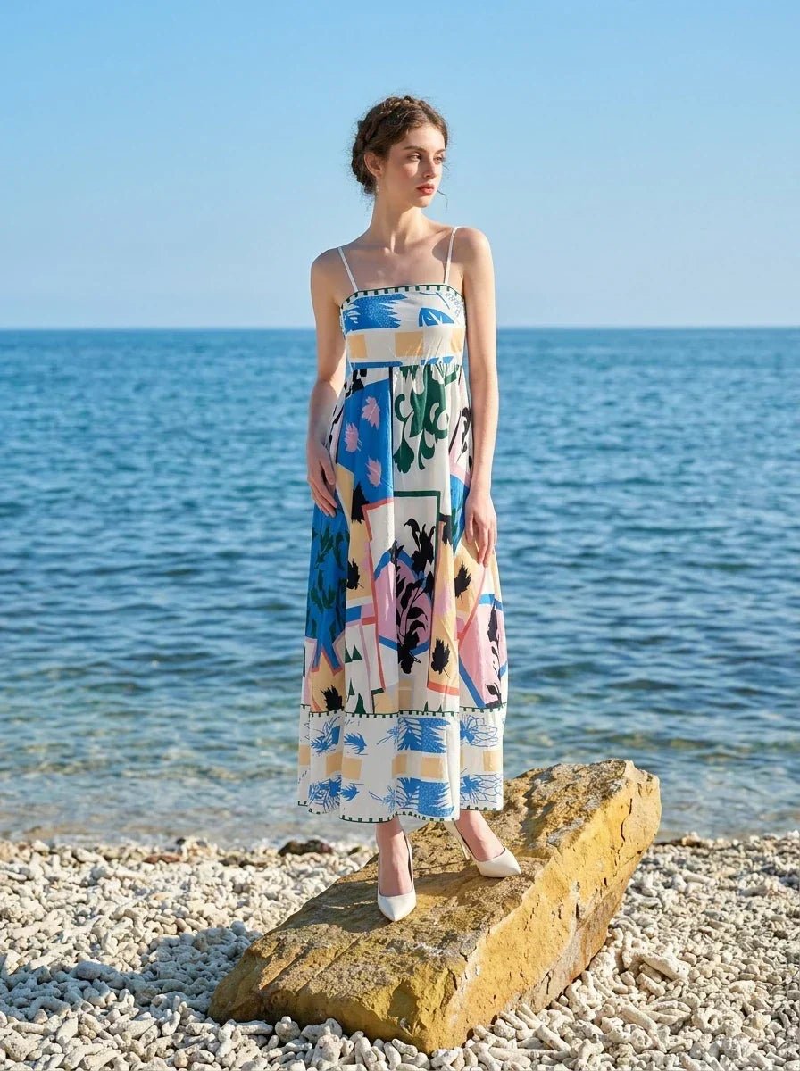 Woman wearing a midi dress with an abstract geometric print standing on a rock by the ocean.