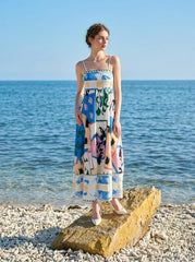 Woman wearing a midi dress with an abstract geometric print standing on a rock by the ocean.