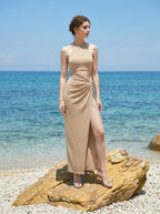 A woman poses on a rock at the beach wearing a champagne halter neck maxi dress with a shimmering appearance.