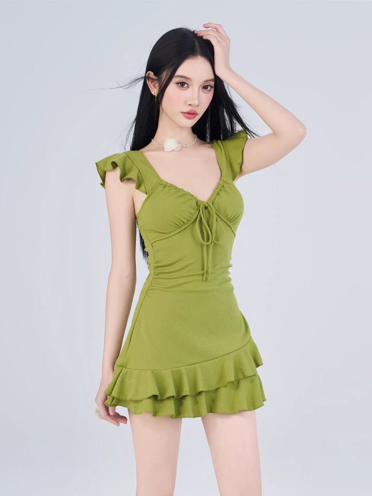 Woman posing in a green ruffled dress, with her hand on her head.