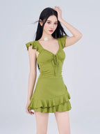 Woman posing in a green ruffled dress, with her hand on her head.