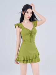 Woman posing in a green ruffled dress, with her hand on her head.