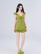 Full-length view of a woman in a green textured dress with ruffled cap sleeves and a tiered hem.