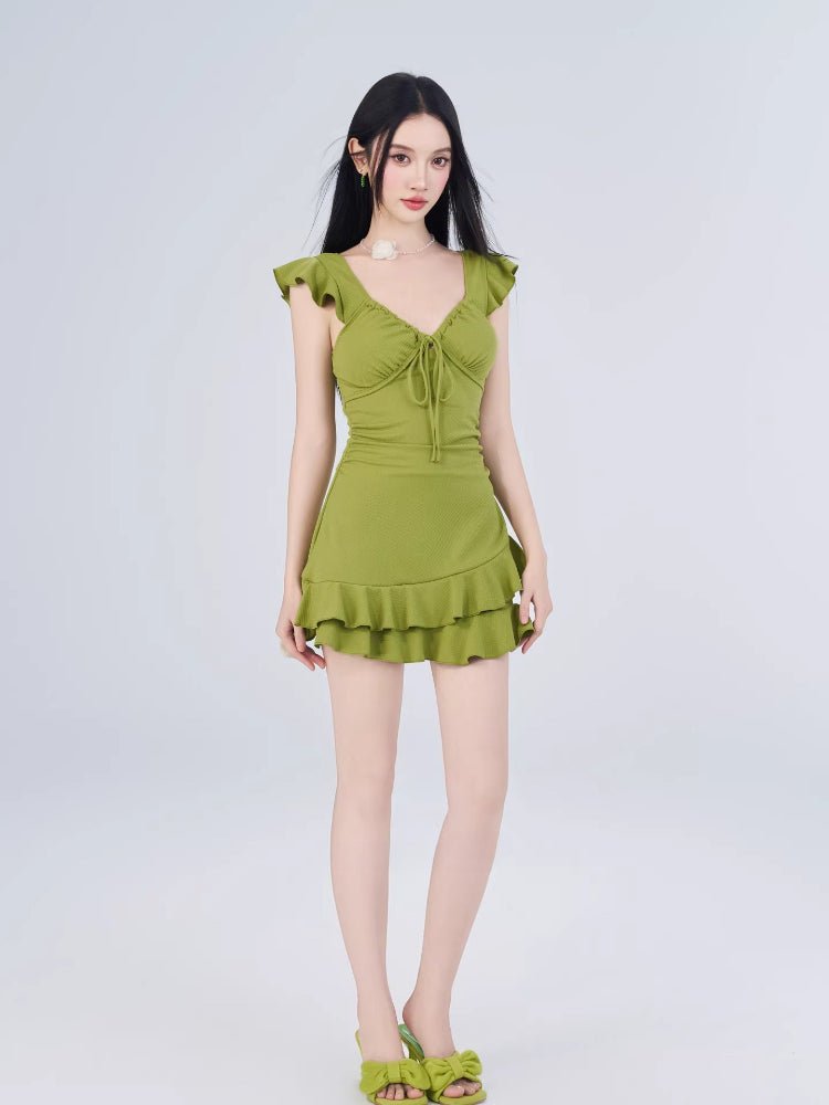 Full-length view of a woman in a green textured dress with ruffled cap sleeves and a tiered hem.