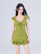 Woman wearing a green A-line dress with ruffled cap sleeves and a tie-front sweetheart neckline.