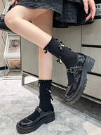 A person's legs and feet in black patent leather Mary Jane shoes with chunky platform soles and black socks with bows and pearls.