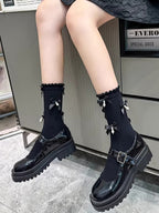 A person wearing black patent leather Mary Jane shoes with chunky platform soles and black socks adorned with bows and pearls.