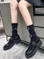 A person wearing black patent leather Mary Jane shoes with chunky platform soles and black socks adorned with bows and pearls.