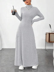 Woman wearing a grey ribbed knit maxi dress with a turtleneck and long sleeves, holding a drink.