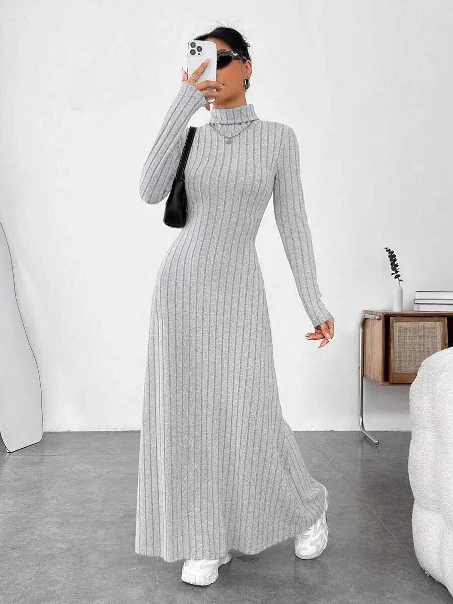 Woman wearing a grey ribbed knit maxi dress with a turtleneck and long sleeves, holding a phone and a handbag.