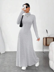 Woman wearing a grey ribbed knit maxi dress with a turtleneck and long sleeves, holding a phone and a handbag.