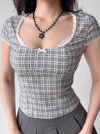 Front view of a woman's torso wearing a gray plaid top with lace trim and a bow detail.