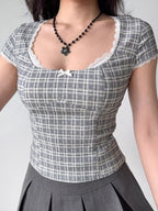 Close-up of a woman wearing a gray plaid short-sleeved top with white lace trim and a small white bow.