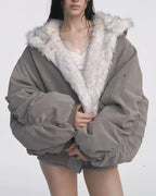 Model wearing a grey bomber jacket with white faux fur lining, hands tucked inside the jacket, white lace-trimmed camisole, and grey shorts.