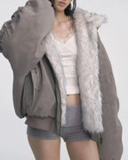 Model wearing a grey bomber jacket unzipped, revealing a white lace-trimmed camisole and grey shorts. One arm is raised.
