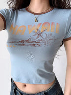 Close-up of a light blue cropped t-shirt with a "Hawaii" graphic print and brown trim.