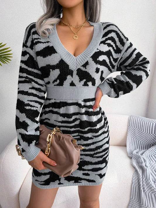 Woman wearing a grey and black tiger print knit mini dress with a V-neck and long sleeves, holding a brown handbag.
