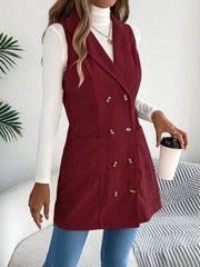 Woman in a burgundy corduroy sleeveless blazer, holding a coffee cup and a handbag.