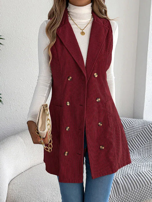 Woman wearing a burgundy corduroy sleeveless blazer over a white turtleneck and blue jeans.