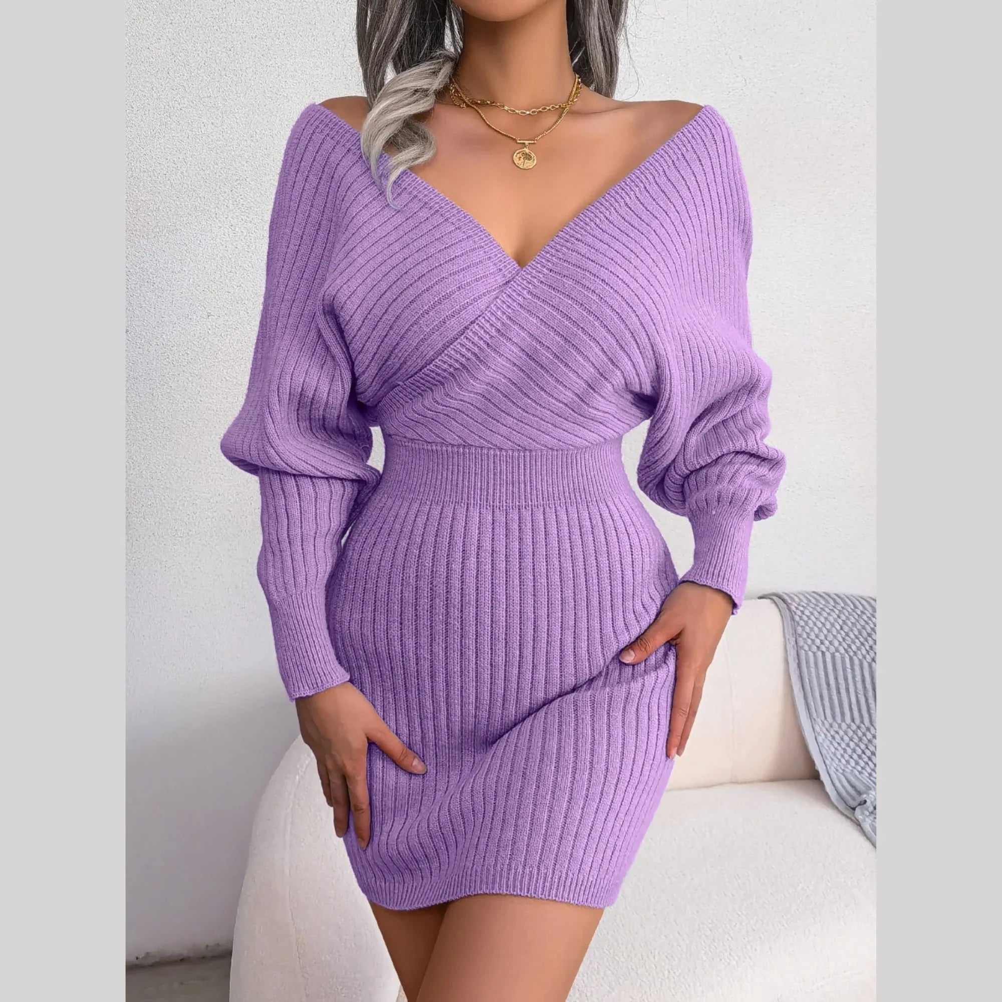 Woman standing in a purple knit mini dress with a V-neck and batwing sleeves.