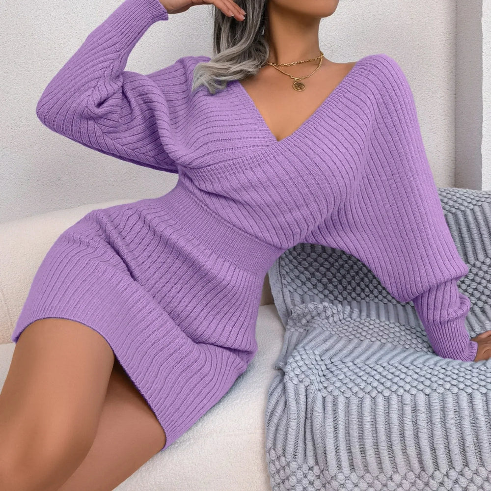 Woman sitting on a couch wearing a purple knit mini dress with a V-neck and batwing sleeves.