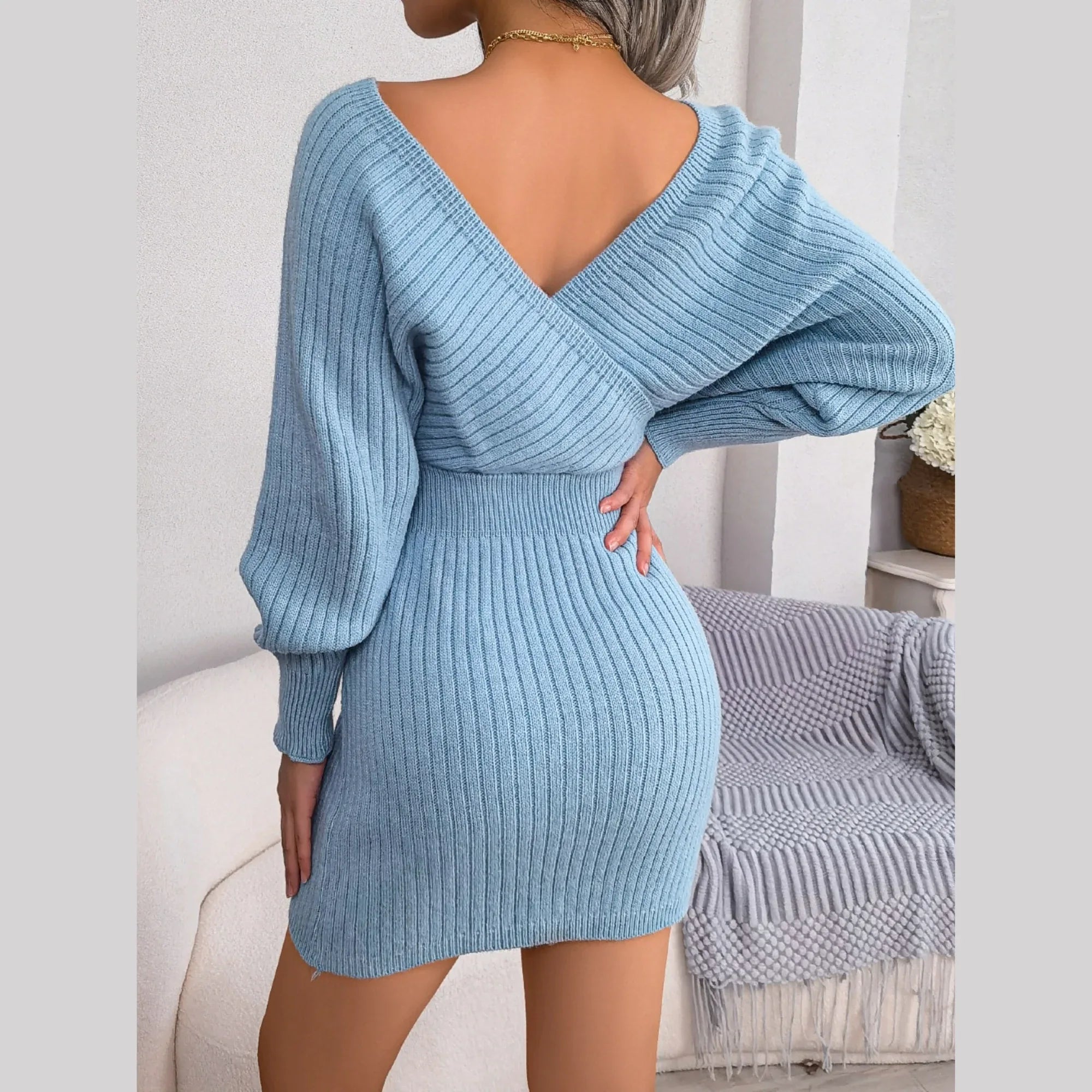 Back view of a woman in a light blue knit mini dress with a V-back and long sleeves.