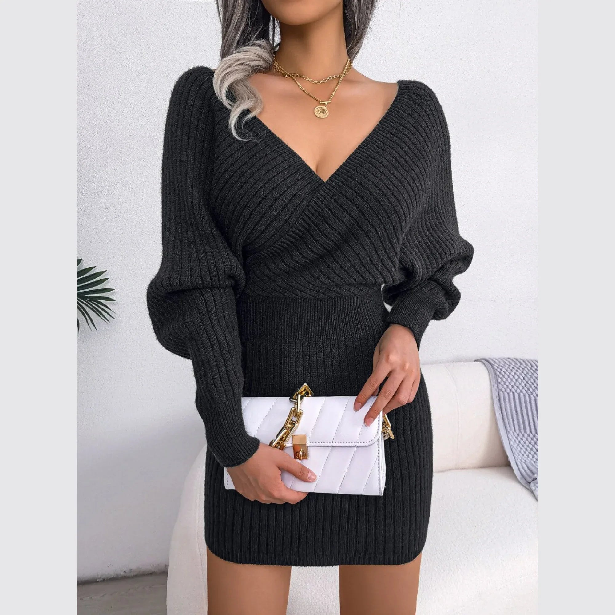Woman holding a white quilted handbag while wearing a charcoal knit V-neck dress.