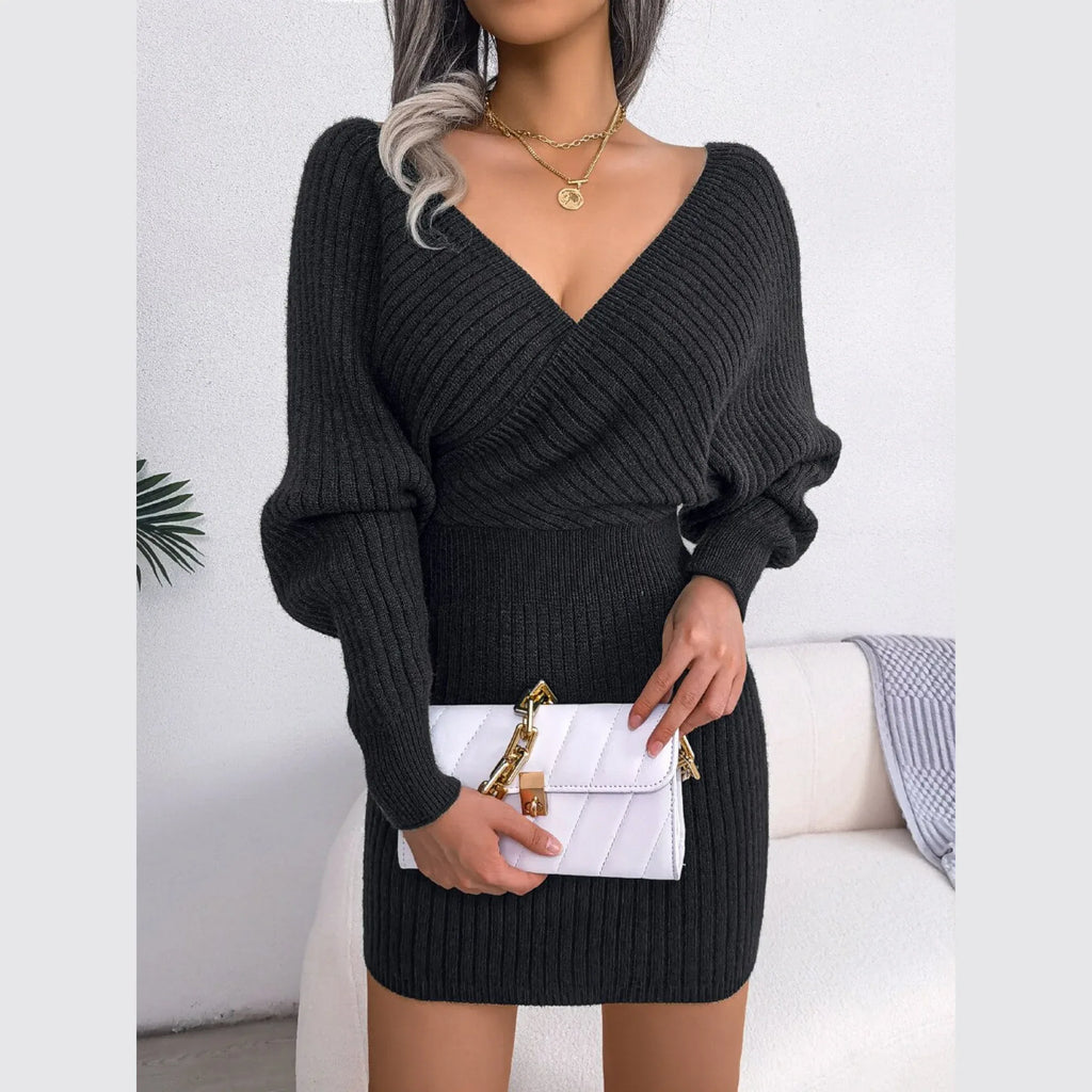 Woman holding a white quilted handbag while wearing a charcoal knit V-neck dress.