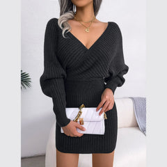 Woman holding a white quilted handbag while wearing a charcoal knit V-neck dress.