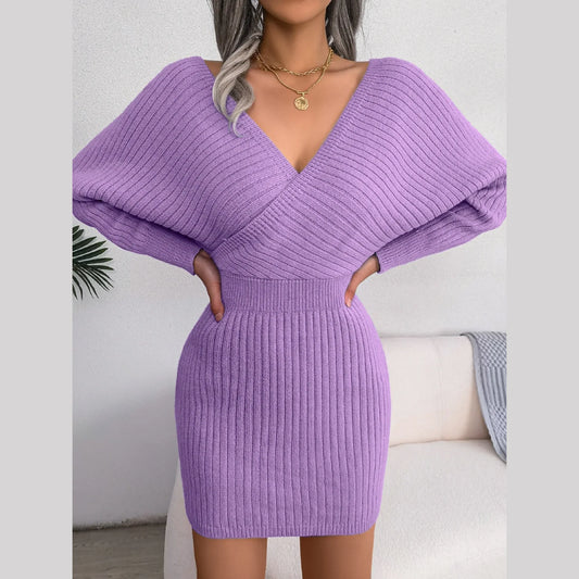Woman in a purple knit dress with a V-neck and batwing sleeves, hands on hips.