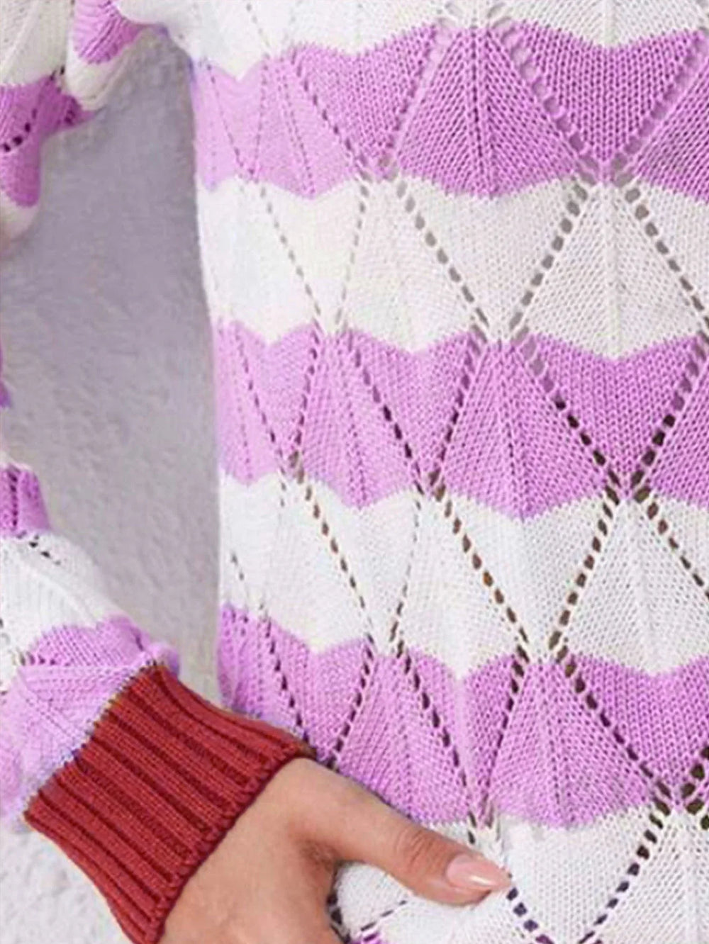 Close-up of the knit texture and geometric pattern of a purple and white striped sweater with a contrast red cuff.