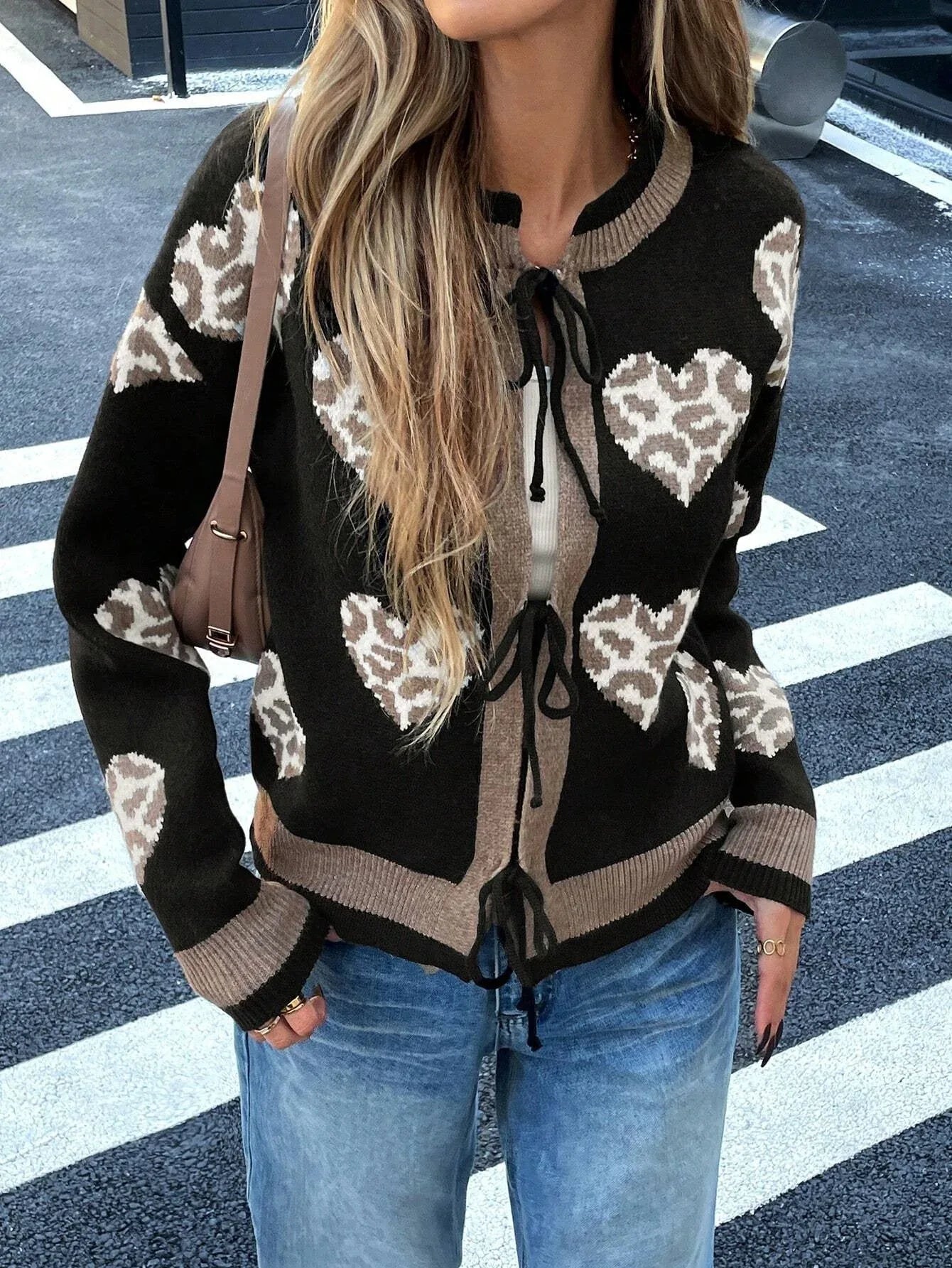Woman wearing a black knit cardigan with a heart and leopard print pattern, tied at the front, paired with blue jeans.