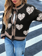 Close-up of a woman's torso wearing a black knit cardigan with a heart and leopard print pattern, tied at the front.