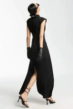 Back view of a model wearing a black sleeveless maxi dress with a high slit and white tie detail