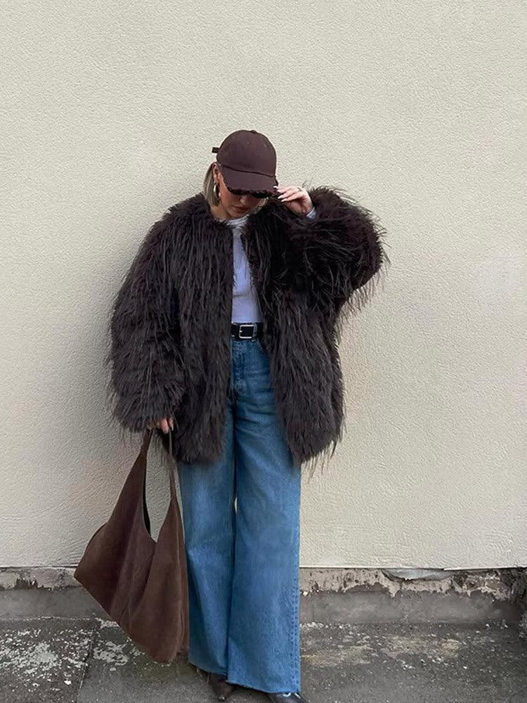 Woman adjusting her sunglasses while wearing a brown shaggy faux fur jacket, blue jeans, and a brown baseball cap.