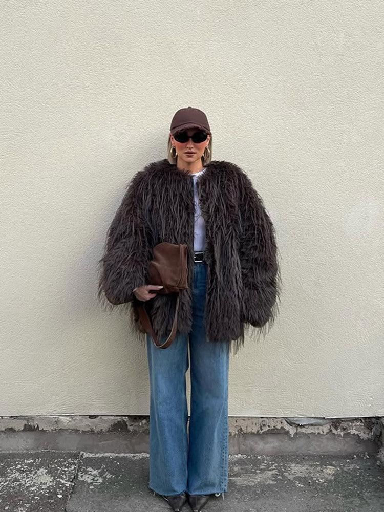 Full body shot of a woman in a brown shaggy faux fur jacket, blue wide-leg jeans, and a brown baseball cap.