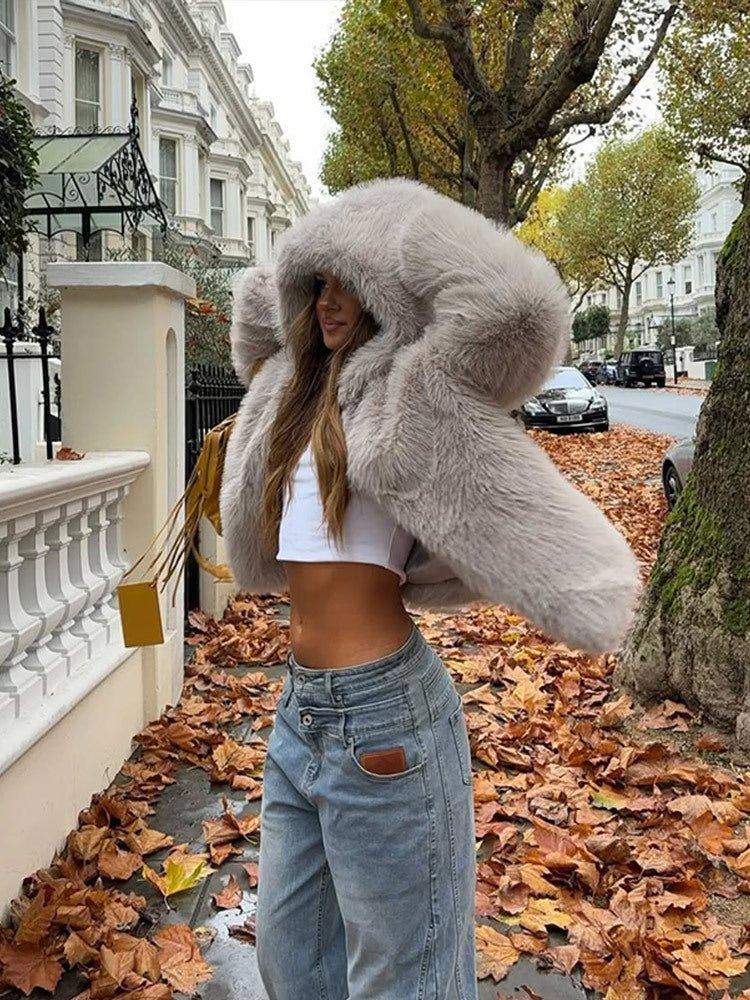 Woman wearing a grey faux fur hooded coat and denim jeans, with autumn leaves on the ground