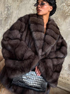 close-up of a woman wearing a brown fur coat with wide lapels and long sleeves, holding a black crocodile-embossed clutch