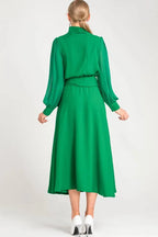 Back view of a woman in a green long-sleeved dress with a midi-length skirt.