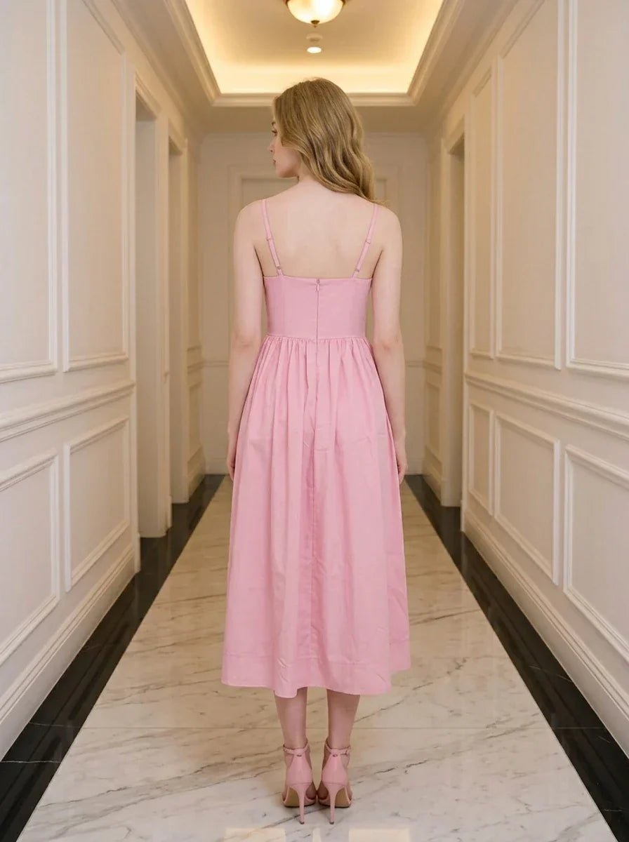 Back view of a woman wearing a pink midi dress with spaghetti straps and a square neckline, standing in a hallway.
