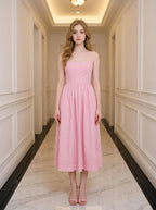 Woman wearing a pink midi dress with spaghetti straps and a square neckline, standing in a hallway.