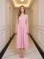 Woman wearing a pink midi dress with spaghetti straps and a square neckline, standing in a hallway.