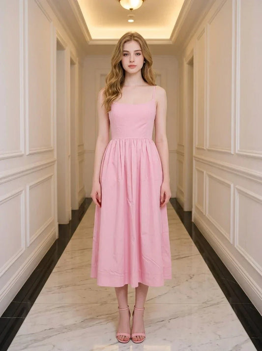 Woman wearing a pink midi dress with spaghetti straps and a square neckline, standing in a hallway.