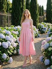 Woman wearing a pink midi dress with spaghetti straps and a square neckline, walking in a garden with hydrangeas.